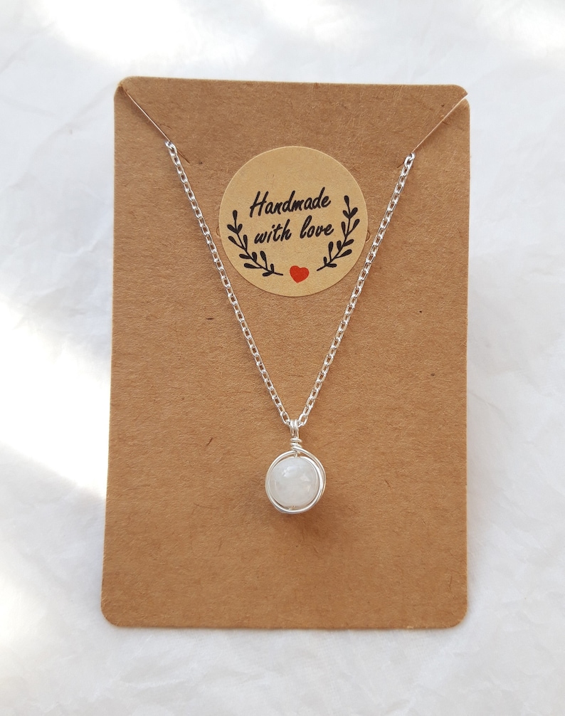May include: A silver chain necklace with a white moonstone pendant on a brown card with a sticker that says "Handmade with love".
