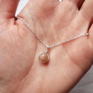 May include: A silver chain necklace with a small, round, light brown gemstone pendant.