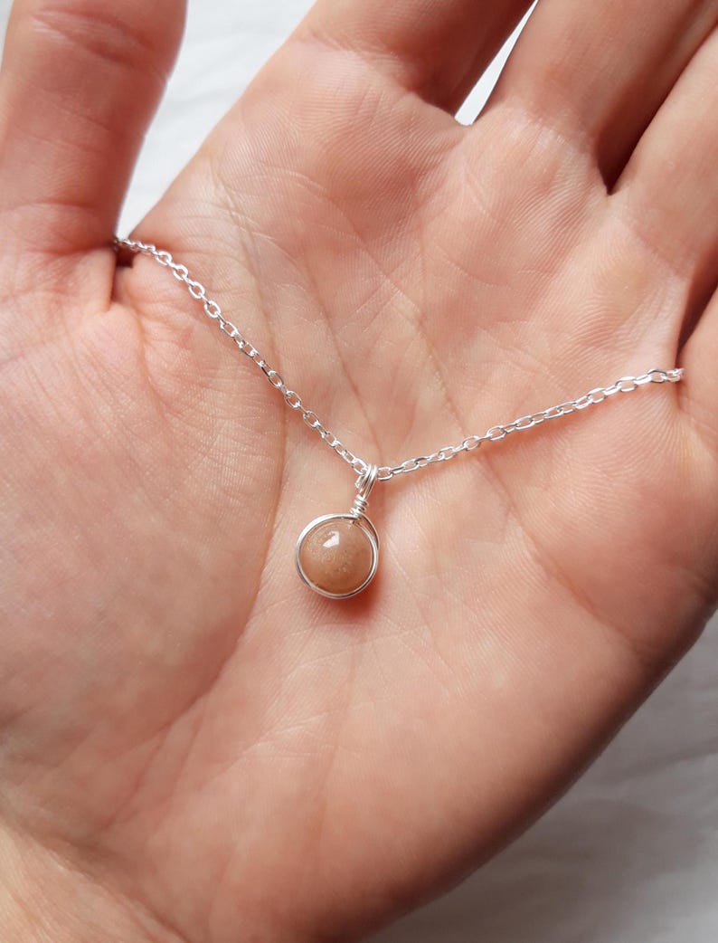 May include: A silver chain necklace with a small, round, light brown gemstone pendant.