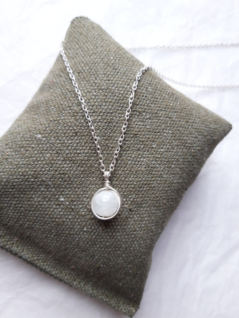 May include: A silver chain necklace with a white moonstone pendant. The pendant is wrapped in silver wire.