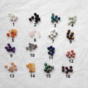 May include: Assortment of 16 different types of beads, each in a separate pile, labeled with numbers 1 through 16. The beads are various colors and shapes, including white, black, blue, green, brown, pink, orange, and purple.