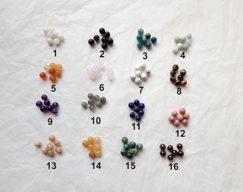 May include: Assortment of 16 different types of beads, each in a separate pile, labeled with numbers 1 through 16. The beads are various colors and shapes, including white, black, blue, green, brown, pink, orange, and purple.