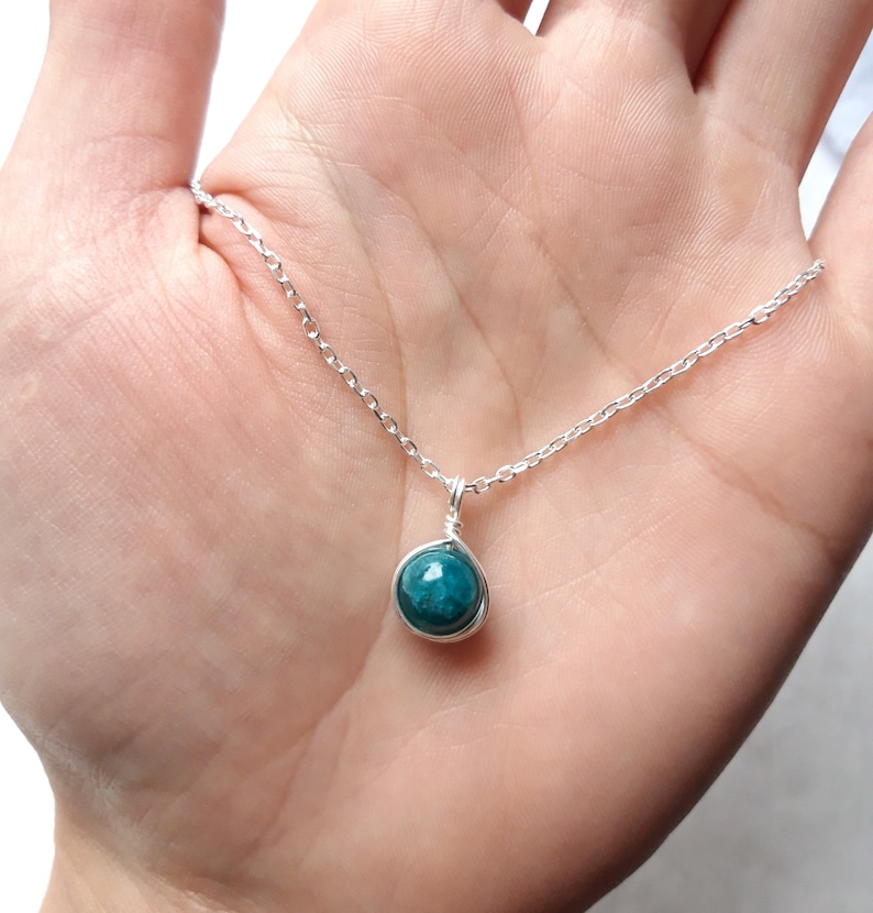 May include: A silver chain necklace with a teal blue gemstone pendant.