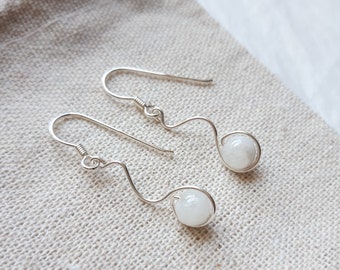 May include: A pair of silver earrings with white gemstone beads. The earrings are made with a simple wire design and have a dangling style.