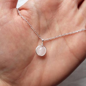 May include: A delicate silver chain necklace with a small, round, light pink rose quartz pendant.