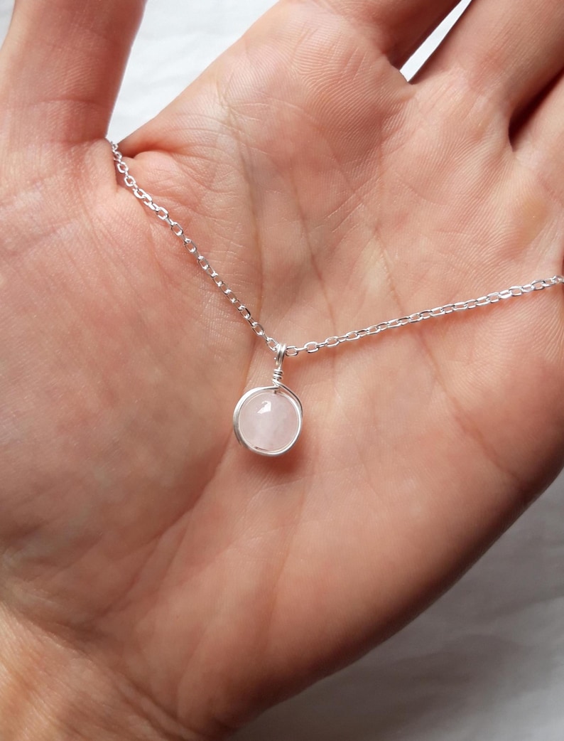 May include: A delicate silver chain necklace with a small, round, light pink rose quartz pendant.
