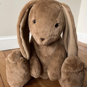 May include: A brown plush bunny rabbit with long floppy ears. The bunny is sitting on a wooden floor.
