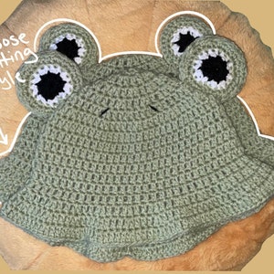 Puede incluir: Sombrero de cubo de crochet verde con orejas de rana. El sombrero tiene un estilo de ajuste holgado.