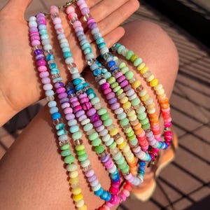 May include: A collection of multiple beaded necklaces featuring round, colorful beads in various shades including pink, blue, green, yellow, and purple. The necklaces are interspersed with clear, transparent spacer beads and feature metallic clasps.