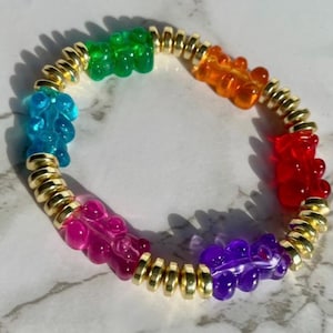 May include: A colorful gummy bear charm bracelet with gold beads. The bracelet features gummy bears in blue, green, orange, red, pink, and purple.