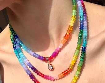 Puede incluir: Un collar de cuentas de varias hileras con cuentas de vidrio translúcido en todo el espectro de colores del arcoíris. El collar incluye un colgante dorado en forma de lágrima con una piedra clara y facetada en la hebra más corta.
