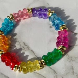 May include: A rainbow gummy bear charm bracelet with gold accents. The bracelet features a variety of colors, including red, orange, yellow, green, blue, and purple.