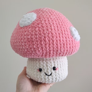 May include: A pink and white crocheted mushroom plush toy with a smiling face. The mushroom has white polka dots on the top.