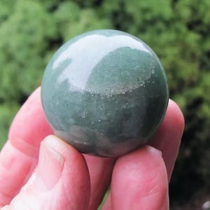 May include: A smooth, green sphere made of polished stone. The sphere has a light green color with a slightly darker green hue in the center. The sphere is about the size of a golf ball.