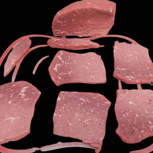 May include: Several raw beef slices, some thick and some thin, are arranged on a red surface. The beef is a light pink color and has a marbled appearance.