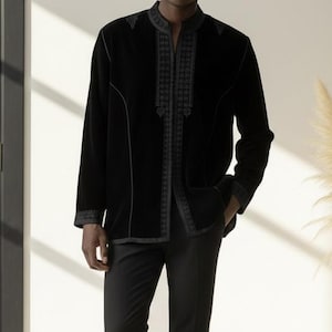 May include: A black velvet jacket with embroidered detailing, worn with black trousers and white trainers. The jacket features a mandarin collar and decorative stitching. The outfit is completed with black trousers and white trainers, creating a modern, stylish look.