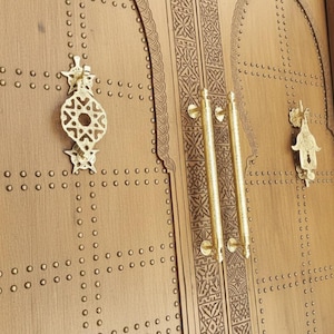 May include: Detailed view of a wooden door with elaborate carvings and brass fixtures. The door has decorative handles and ornate door knockers. The wood is a warm, natural colour, and the brass hardware adds a touch of elegance.