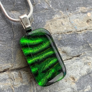 Puede incluir: Un colgante de vidrio verde con una cadena de plata. El vidrio tiene un patrón de remolino y un acabado brillante.