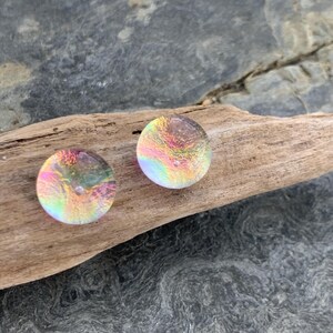 Puede incluir: Dos cabujones redondos de vidrio iridiscente con efecto arcoíris. Los cabujones están colocados sobre un trozo de madera flotante. Los colores cambian de rosa a amarillo, verde y azul, creando un efecto brillante. Adecuado para la creación de joyas.