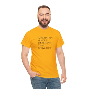 Pode incluir: T-shirt amarelo mostarda com o texto "IMAGINATION IS MORE IMPORTANT THAN KNOWLEDGE" em preto. A t-shirt é de gola redonda e está a ser usada por uma pessoa.