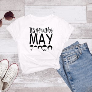 May include: White t-shirt with black text that reads "It's gonna be MAY" with a row of five black silhouettes of people's heads below the text.