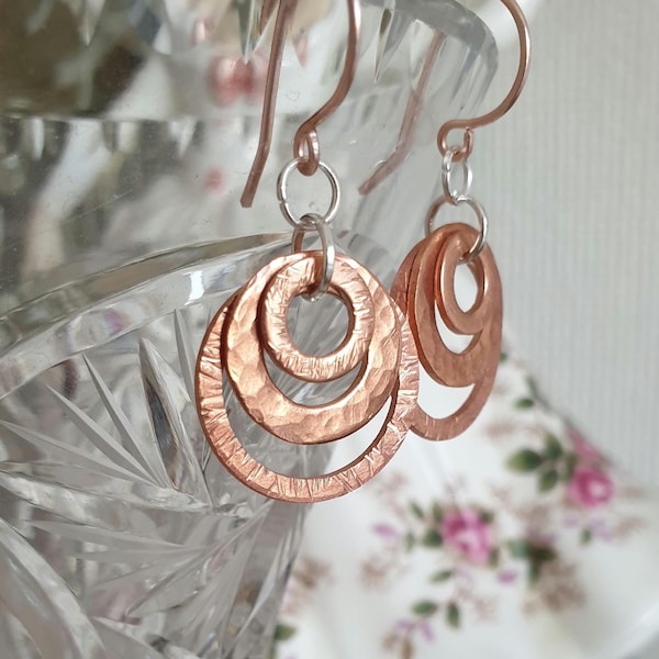 Petite hammered earrings featuring copper concentric circles hanging from real rose gold ear hooks.