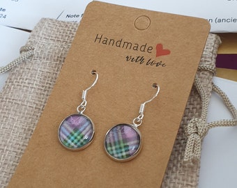 May include: A pair of silver dangle earrings with a round, green, pink and white tartan design. The earrings are handmade and come in a small hessian bag with a brown paper tag that says "Handmade with love".