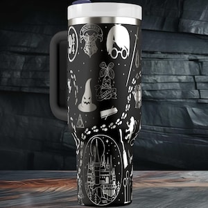 Puede incluir: Taza de viaje negra con tapa y asa blancas, con ilustraciones blancas de un tema de escuela de magia. El diseño incluye un sombrero seleccionador, gafas, un castillo y otros iconos relacionados. La taza tiene una pajita y está sobre un fondo oscuro.