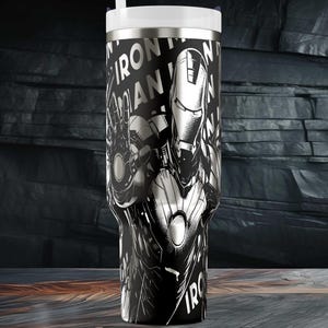 May include: Black and white tumbler featuring Iron Man. The design includes the Iron Man character and the words "IRON MAN" in a bold, stylized font. The tumbler has a white lid and a straw.