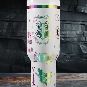 Könnte beinhalten: Weißer Becher mit Deckel und Strohhalm, mit einem holografischen Design mit dem Wort "Hogwarts" und anderen Grafiken. Der Becher hat einen regenbogenfarbenen Rand und ist mit verschiedenen Symbolen und Texten verziert.