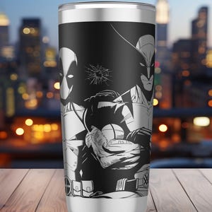 Puede incluir: Vaso térmico de acero inoxidable con una ilustración en blanco y negro de Deadpool y Wolverine. El diseño incluye un efecto de cristal roto e imágenes de superhéroes. El vaso tiene tapa y base plateadas.