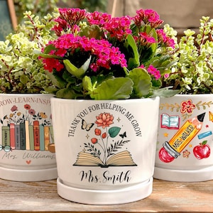 May include: Three white ceramic flower pots with saucers, each filled with plants and vibrant flowers. The pots are decorated with educational themes, including books, pencils, and the text "GROW-LEARN-INSP", "THANK YOU FOR HELPING ME GROW", and "MRS. WALKER".
