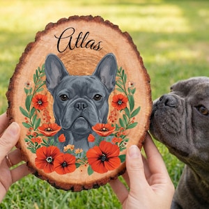 May include: A wooden slice featuring a portrait of a gray French Bulldog named Atlas, surrounded by red poppy flowers and green leaves. The dog's portrait is centered on the wood, with the name Atlas written in elegant script above.