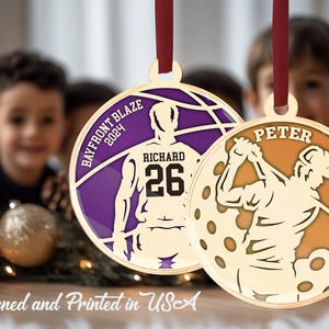 May include: Two gold-coloured Christmas ornaments featuring a basketball player and a golfer. The basketball ornament is purple with the text "BAYFRONT BLAZE 2024" and "RICHARD 26". The golf ornament is orange with the text "PETER GOLF CLUB 2024".