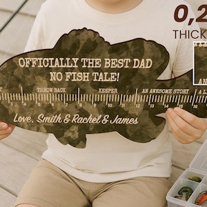 May include: A fish-shaped wooden ruler with a camouflage pattern, measuring 0.64 cm in thickness. It features the text "OFFICIALLY THE BEST DAD NO FISH TALE!" and "Love, Smith & Rachel & James," along with markings for bait, throw back, keeper, and stories.