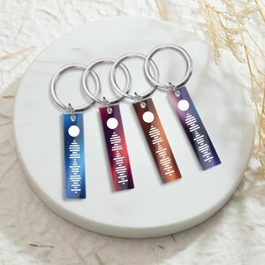 May include: Four silver keychains with colorful rectangular tags featuring a white sound wave design. The tags have a gradient of blue, red, purple, and orange.