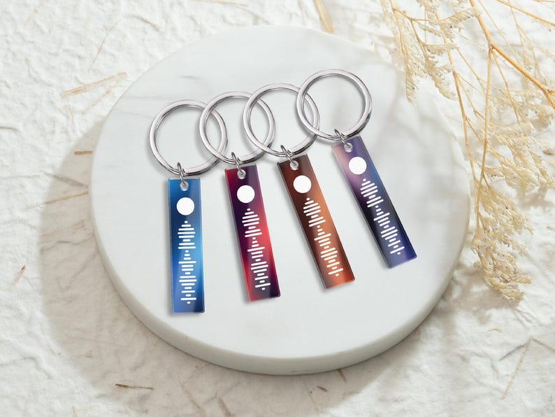 May include: Four silver keychains with colorful rectangular tags featuring a white sound wave design. The tags have a gradient of blue, red, purple, and orange.