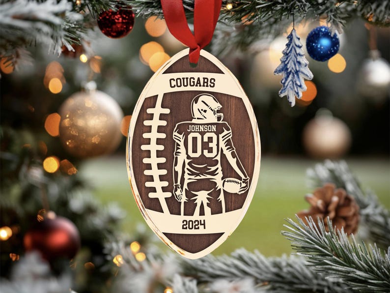 May include: A brown wooden football bauble with a gold outline. The bauble features a football player in a black uniform with the number "03" on the back. The text "COUGARS" and "JOHNSON" are also on the bauble, along with the year "2024".