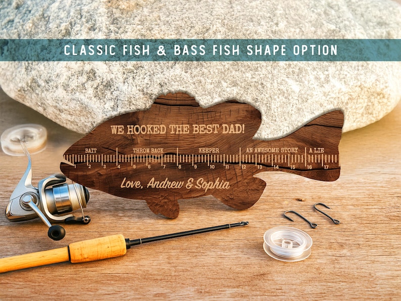May include: A wooden fish-shaped ruler with a dark wood grain finish, featuring the text WE HOOKED THE BEST DAD! and Love, Andrew & Sophia. The ruler includes markings from 1 to 17 inches with labels for bait, throw back, keeper, an awesome story, and a lie.