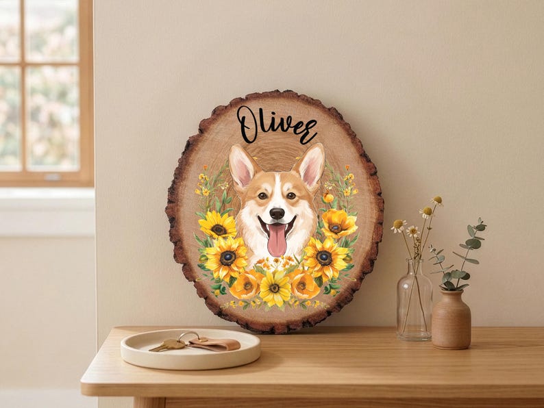 May include: A wooden plaque with a corgi illustration surrounded by sunflowers. The corgi has a happy expression with its tongue out. The name "Oliver" is written above the corgi in black script.