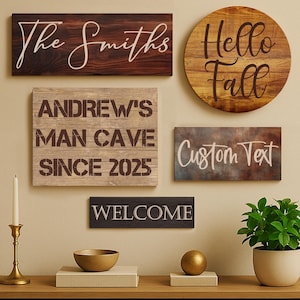 May include: A collection of wooden signs with various text, including "The Smiths", "Andrew's Man Cave Since 2025", "Hello Fall", "Custom Text", and "Welcome". A candle holder, bowl, and plant are on a wooden table.
