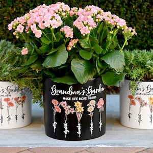 May include: Three ceramic flower pots with plants. The center pot is black with the text "Grandma's Garden MAKE LIFE MORE GRAND". The other two pots are white with the text "Grandma's Garden LOVE GROWS HERE". Each pot has floral illustrations.
