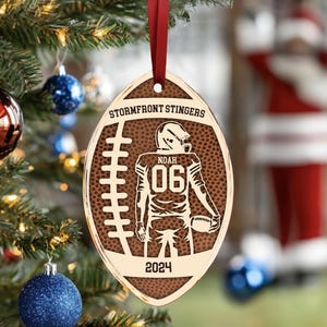 May include: A brown and gold football-shaped Christmas bauble with the text "Stormfront Stingers" and "Noah 06 2024" on it.