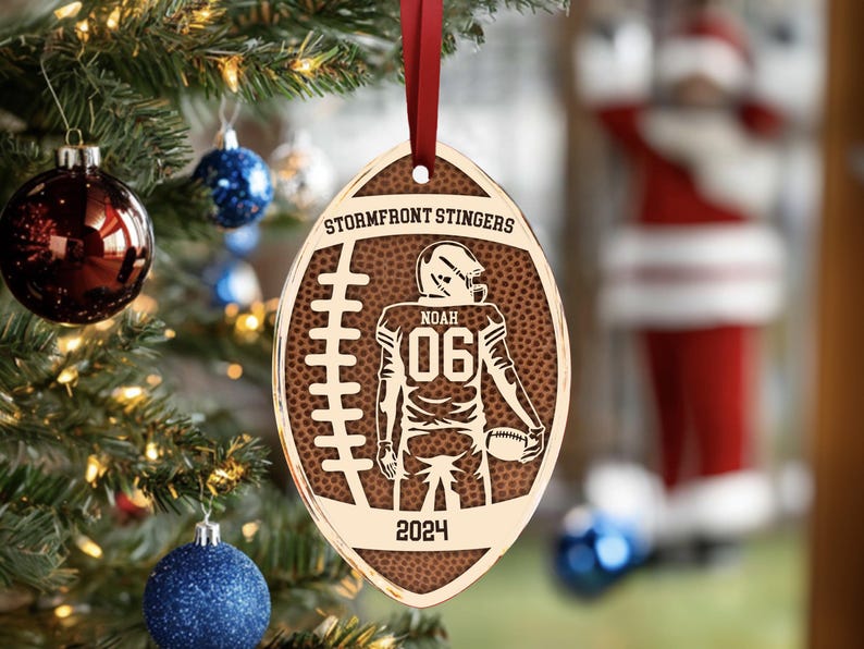 May include: A brown and gold football-shaped Christmas bauble with the text "Stormfront Stingers" and "Noah 06 2024" on it.