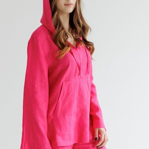 May include: A bright pink linen hoodie and matching shorts set. The hoodie has a drawstring hood and a large pocket on the front. The shorts have a relaxed fit.