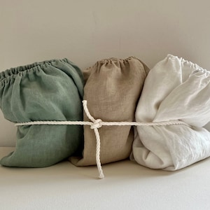 May include: Three fabric drawstring bags in different colors: green, beige, and white. The bags are tied together with a white rope.