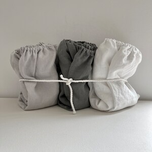 May include: Three linen fabric bundles tied together with a white rope. The bundles are in shades of gray, white, and light gray.