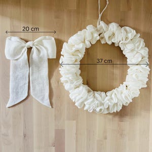 Puede incluir: Una corona de tela blanca con un di&aacute;metro de 37 cm y un lazo de tela blanca a juego de 20 cm de ancho.