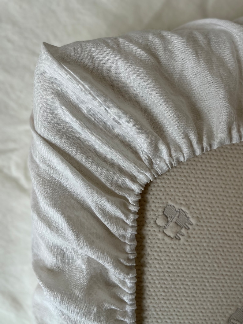 May include: Close-up of a white linen fitted sheet with elastic edging. The sheet is made of a soft, natural fabric and is perfect for a comfortable night's sleep.