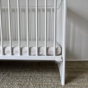 May include: White wooden crib with a white and pink striped mattress. The crib is on a light brown carpet.